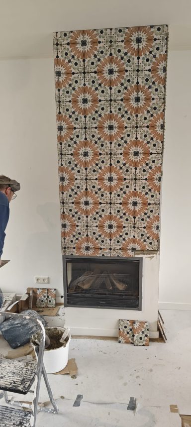 Witte muur met een betegelde schouw met kleurrijke, geometrische patronen.